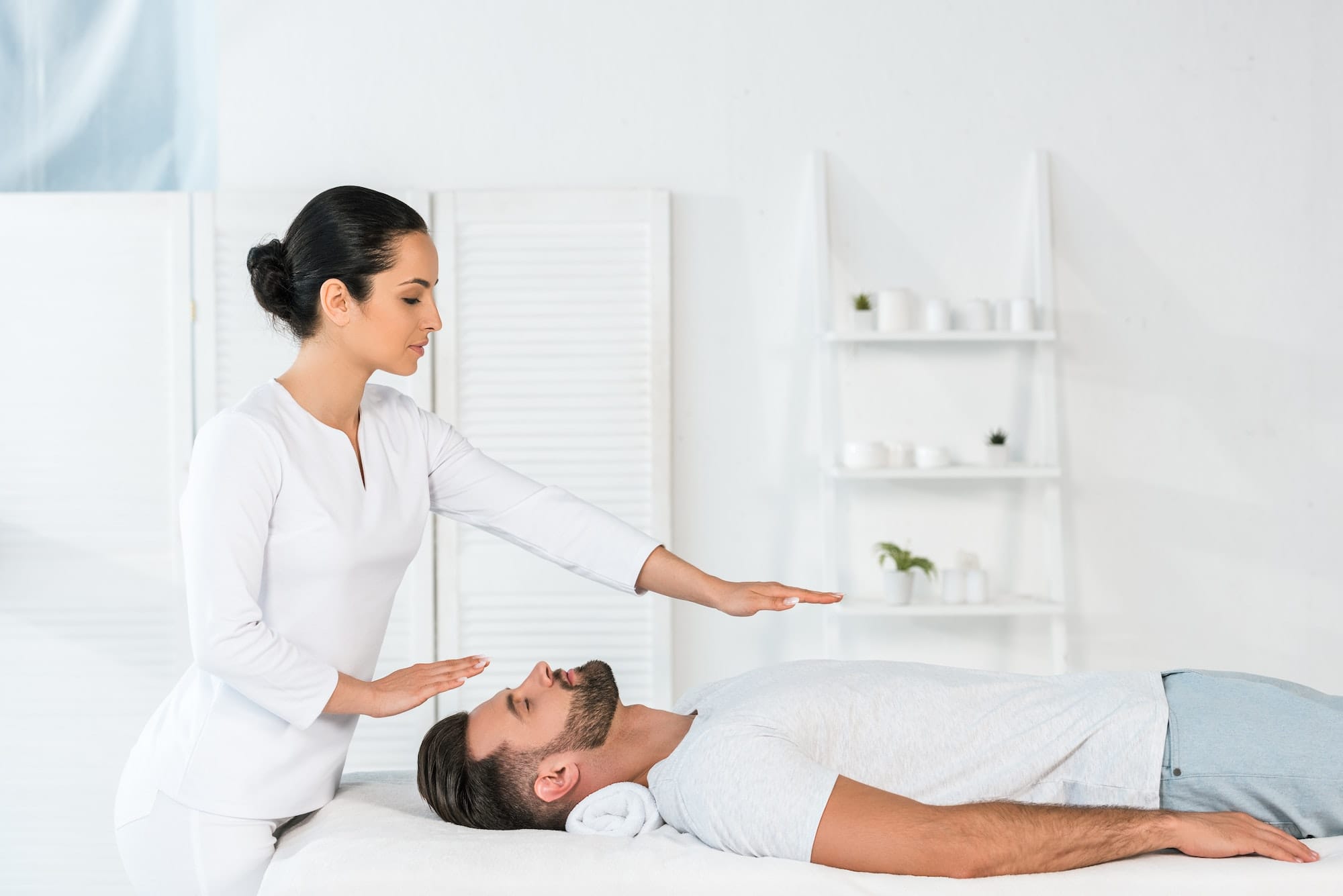 attractive healer putting hands above body of handsome man on massage table